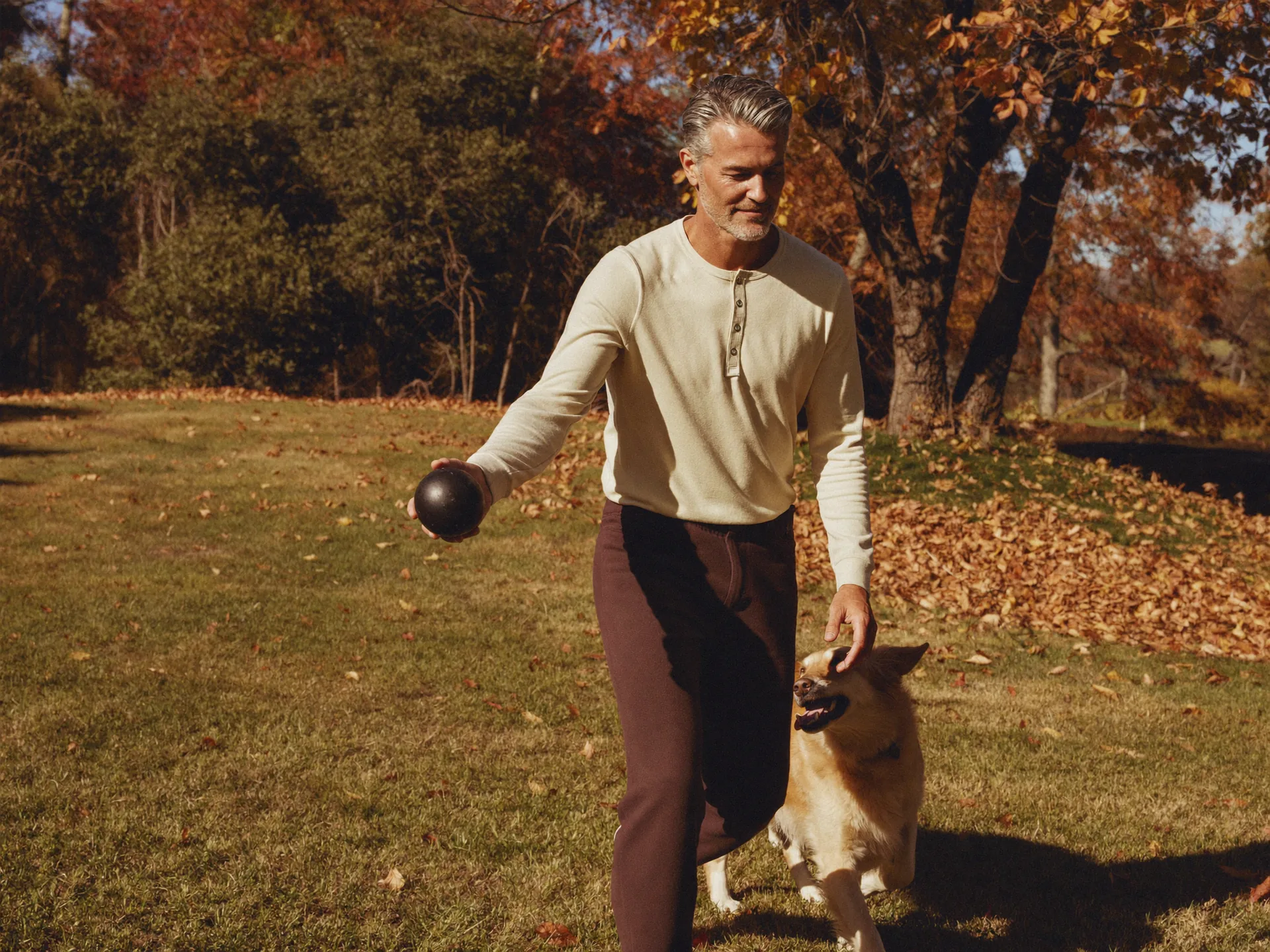 A man in his early fifties playing fetch with a golden retriever in an autumn backyard — the active, present family life behind a hormone-optimization plan