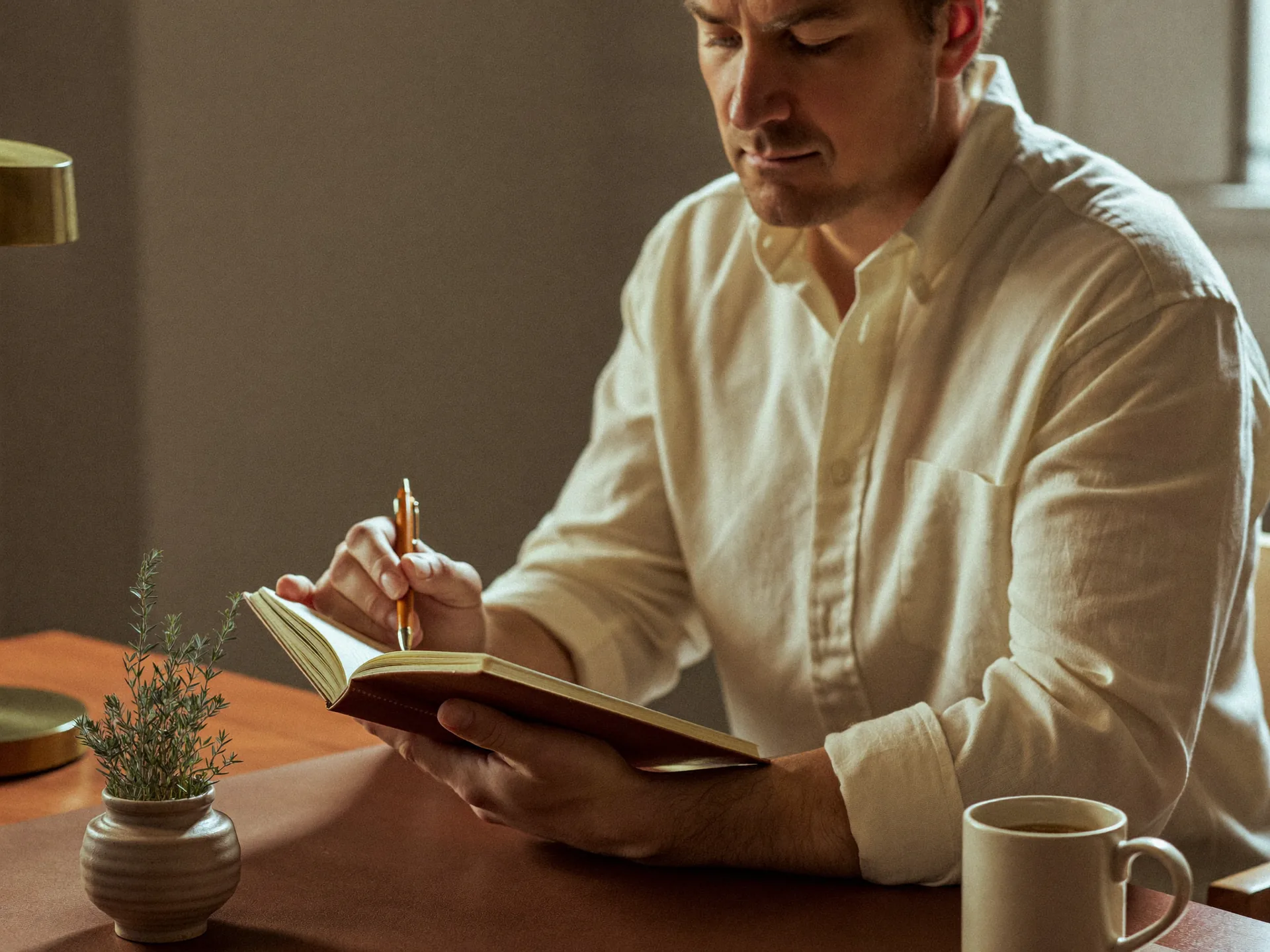 A man writing in a leather notebook at a wooden desk — focused, even-keeled, the kind of clarity a hormone-optimization program supports